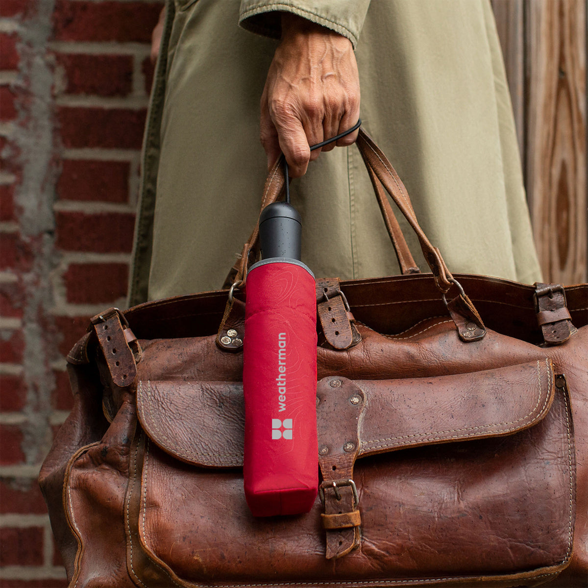 Person walking with closed Weatherman Travel Umbrella in red in their hand.