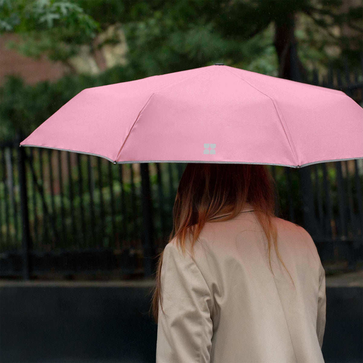 Woman walking down the street while holding an opened Weatherman Travel Umbrella in blush.