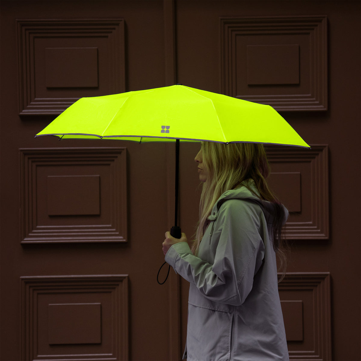 Woman walking with opened Weatherman Travel Umbrella in neon yellow.